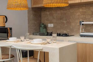 Uma cozinha com parede de pedra, bancada de madeira e luminária de vime suspensa.