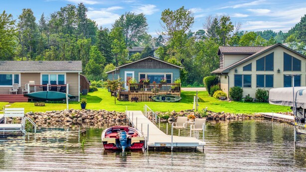 A lakeside property with a dock, a small boat, and a house with a deck. - Cozy 2-bedroom cottage on Lake Bemidji with AC (Bemidji)