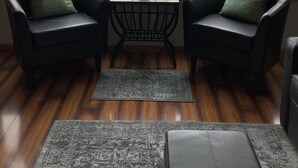 A room with two leather chairs, a small table with a plant, and a view of a lake through large windows. - Cozy 2-bedroom cottage on Lake Bemidji with AC (Bemidji)