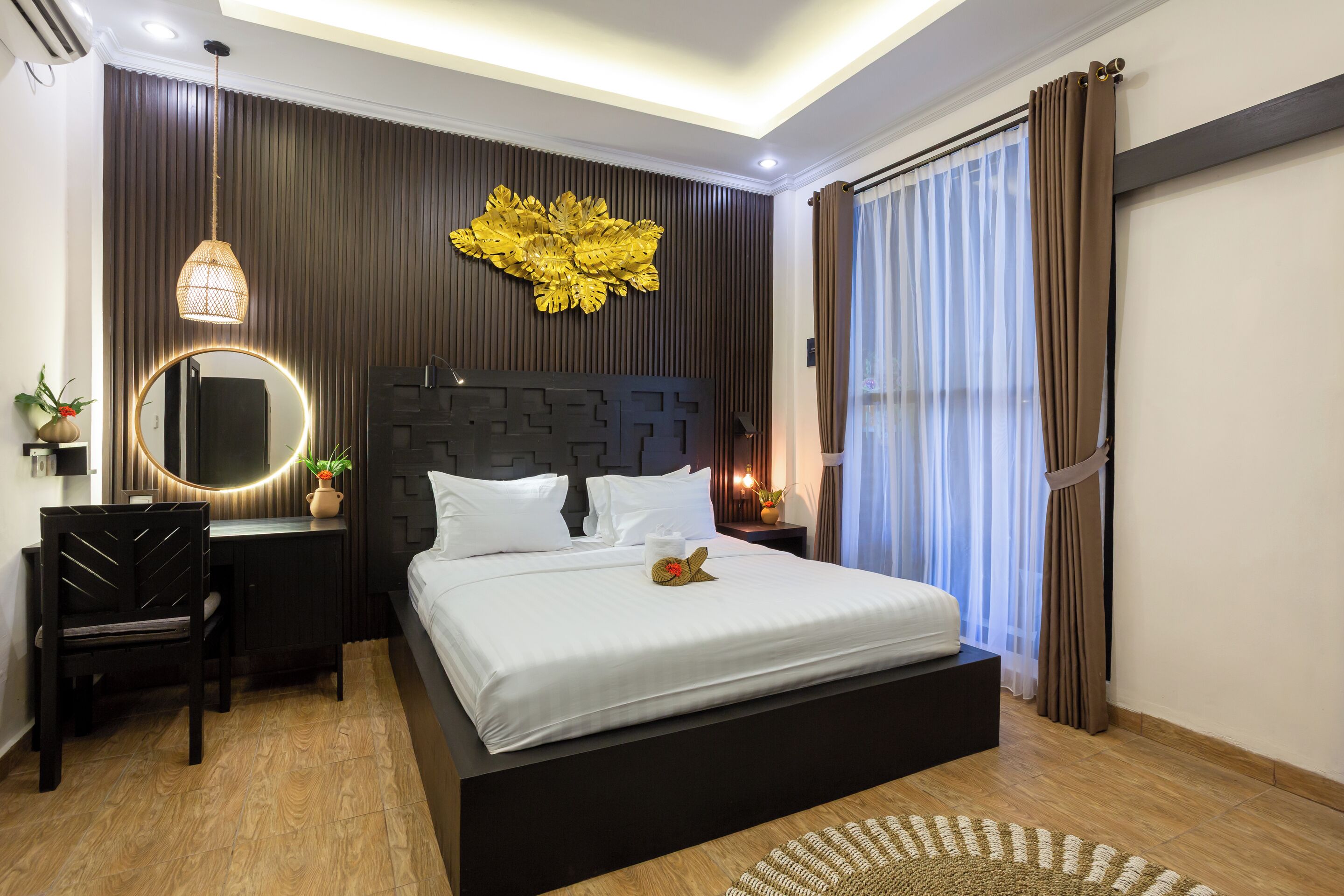 A modern bedroom with a large bed, a desk, a chair, a round mirror, and a decorative wall piece.