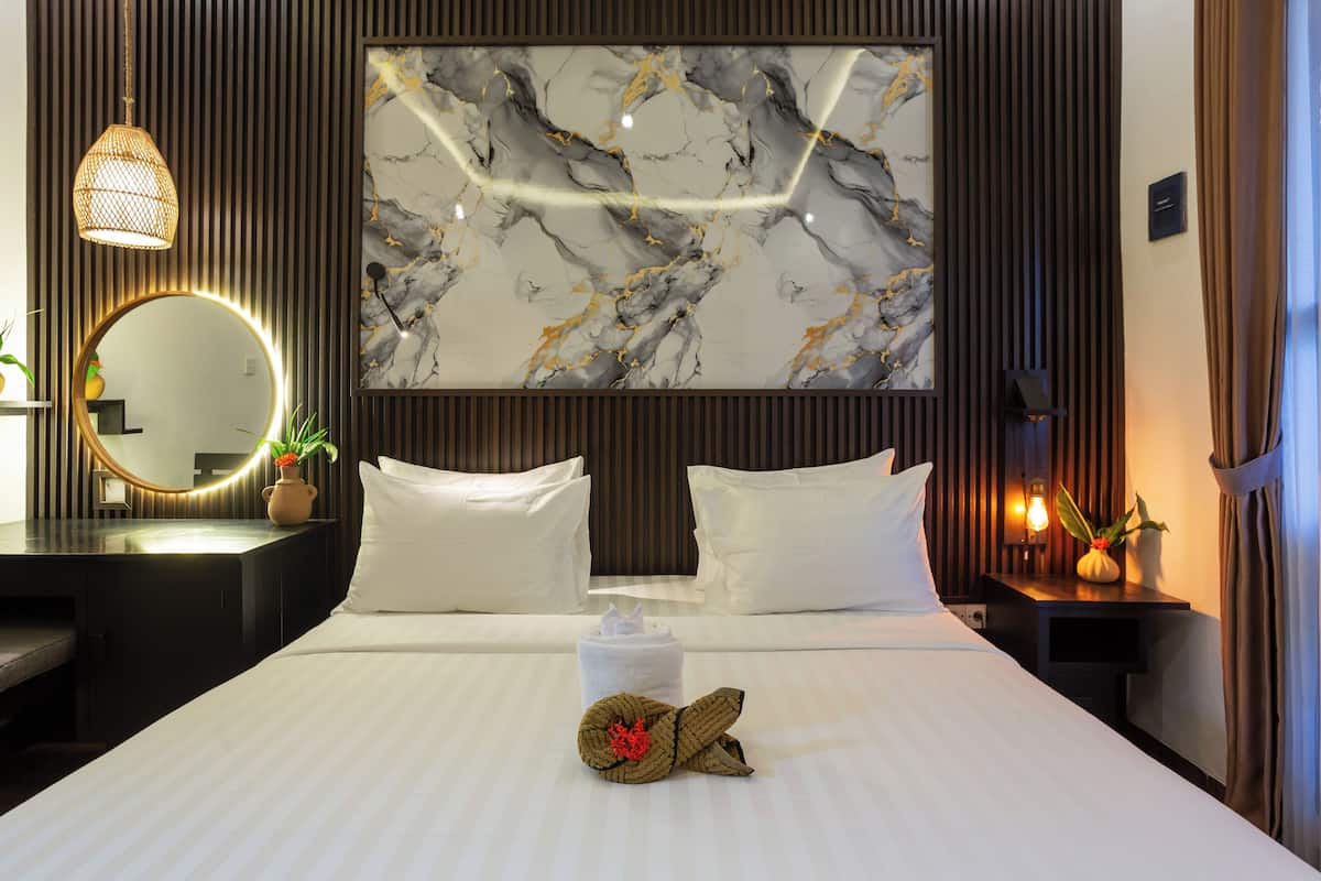Habitación de hotel con una cama, un espejo redondo, una pared de mármol y una mesita de noche con una planta.
