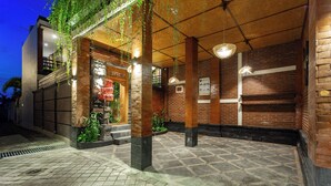 Un bâtiment à la façade en briques, doté d’un espace d’entrée abrité avec des lampes suspendues et d’un sol carrelé.