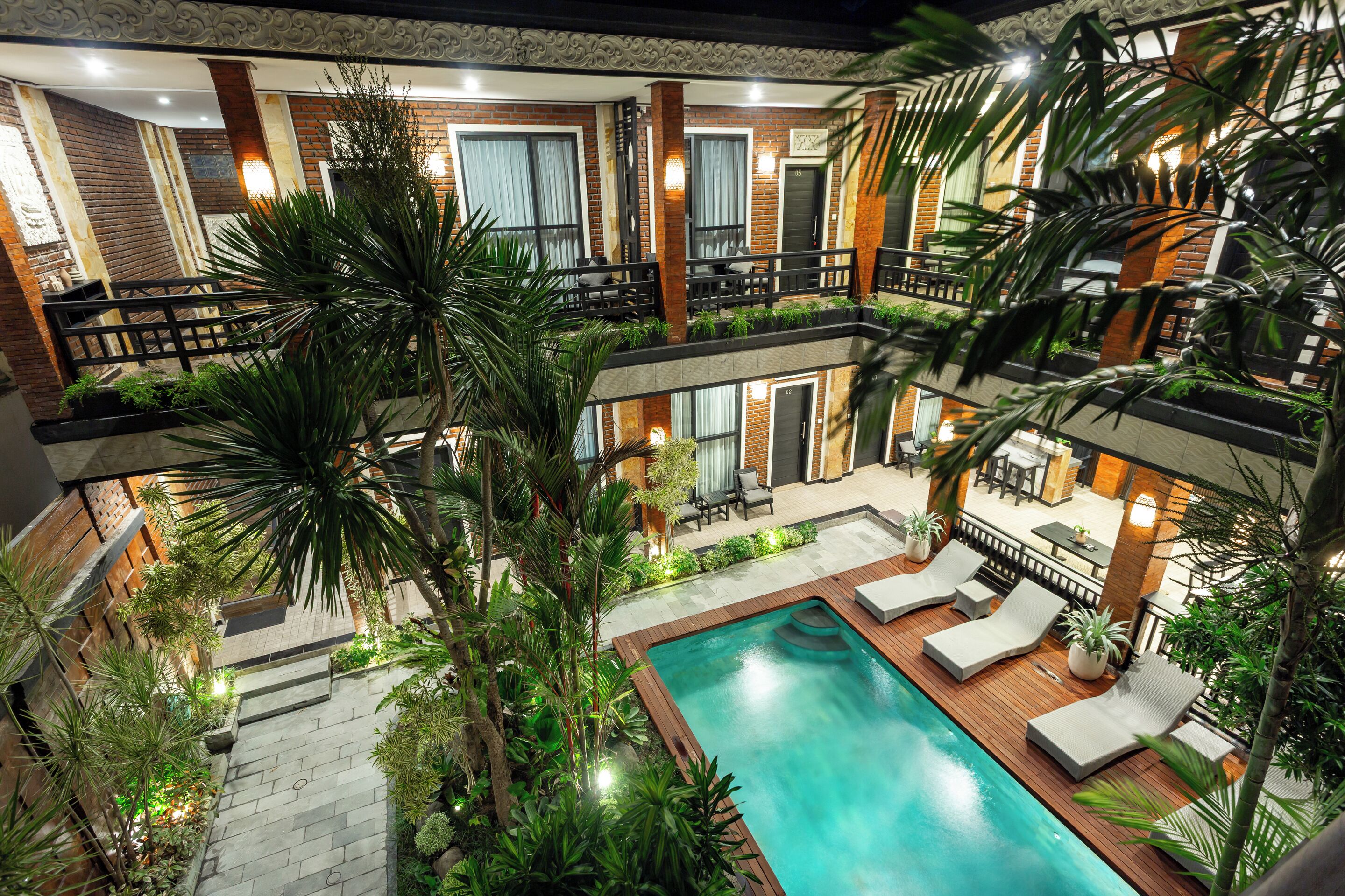 A multi-level outdoor pool area with a wooden deck, lounge chairs, and potted plants.
