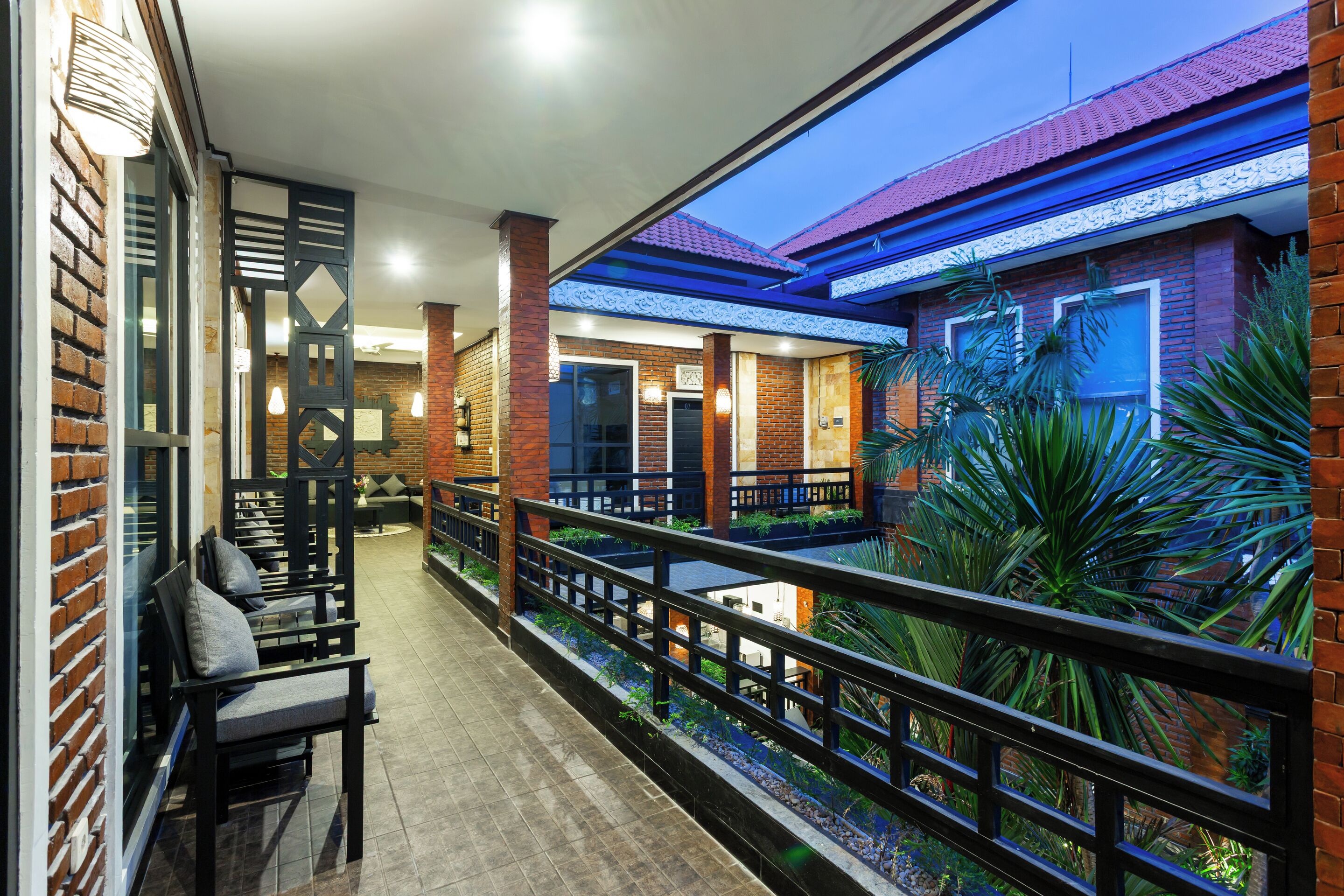 A covered outdoor seating area with brick walls, a railing, and a view of the building's interior.