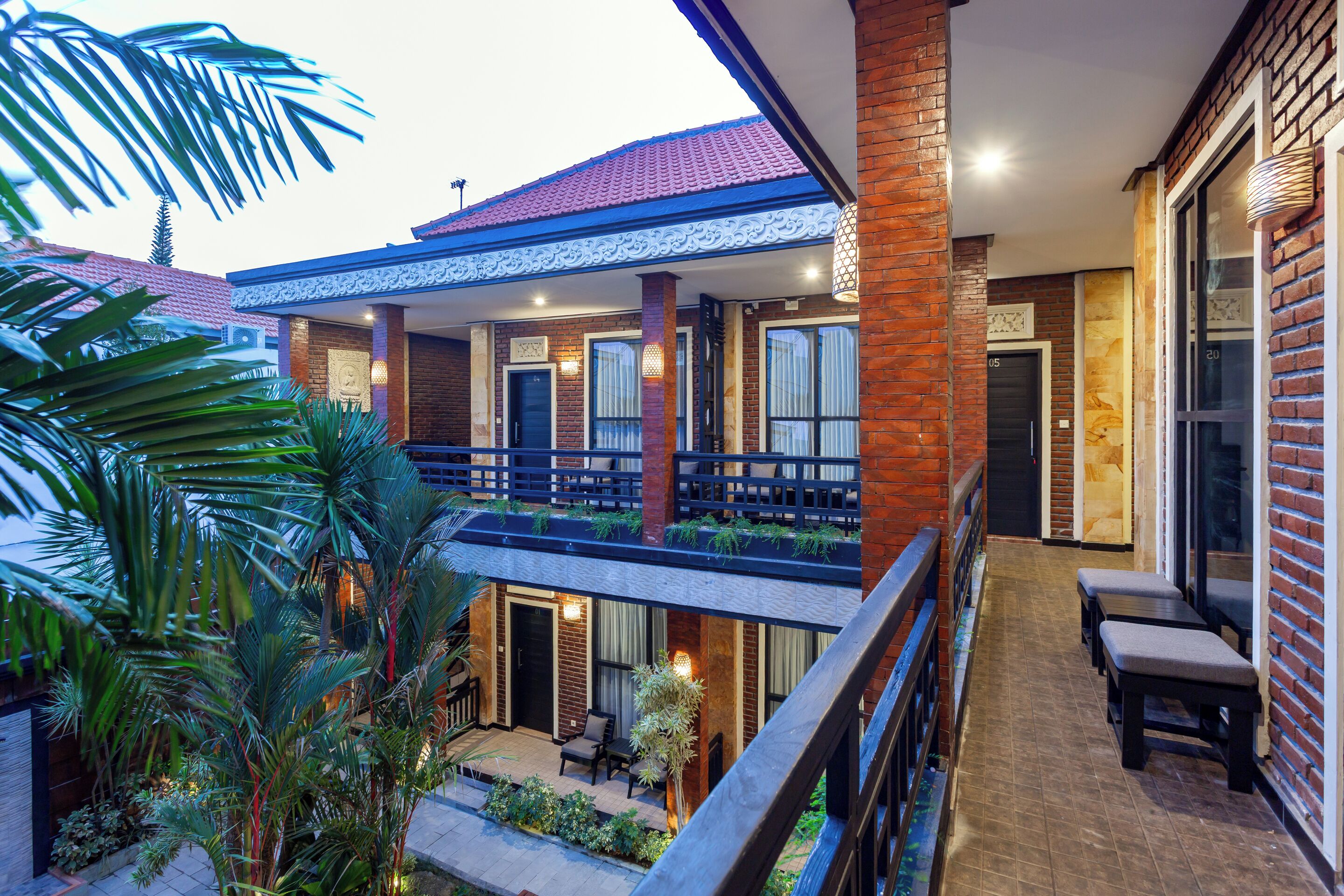 A hotel with a covered outdoor seating area, a balcony with plants, and a brick facade.