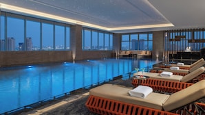 A modern indoor swimming pool with clear views of the city skyline, lounge chairs with towels, and a starry ceiling. - Holiday Inn Shijiazhuang High-tech Zone (Shijiazhuang)
