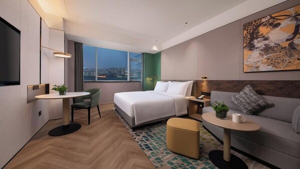 A modern hotel room with a bed, a desk, a sofa, a small table, and a large window with a city view. - Holiday Inn Shijiazhuang High-tech Zone (Shijiazhuang)