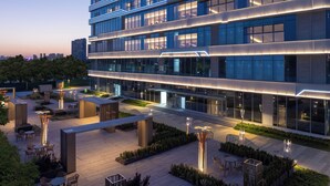 A modern building with multiple floors, large windows, and a well-lit outdoor area with seating and plants. - Holiday Inn Shijiazhuang High-tech Zone (Shijiazhuang)