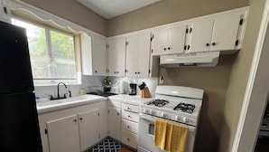 Una cocina con armarios blancos, estufa, fregadero y ventana con persianas.