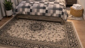 A bedroom with a checkered bedspread, a wooden headboard, a nightstand with a lamp, a potted plant, and a decorative rug.