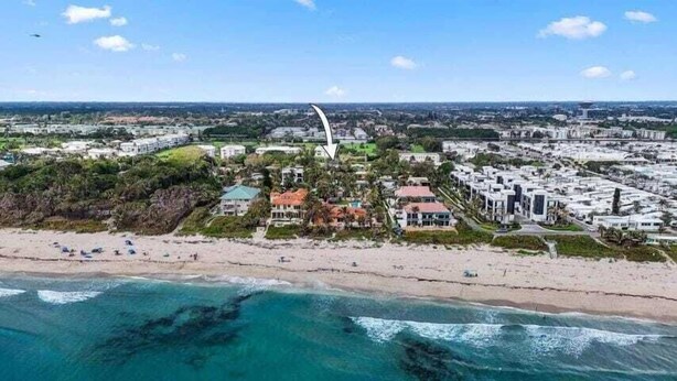 Vista aérea de un pueblo costero con propiedades frente a la playa, una estructura blanca curvada destacada, y una combinación de edificios residenciales y comerciales.