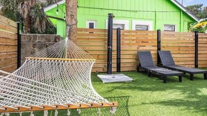Una hamaca, dos sillones de descanso, un edificio verde y una valla de madera en un patio trasero.