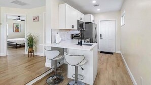 Cocina moderna con armarios blancos, un refrigerador de acero inoxidable y dos taburetes de bar.