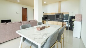 A modern living room with a sofa, a dining table with chairs, a kitchen area, and a ceiling fan.