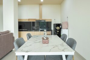 A modern kitchen with a dining area, including a marble table, grey chairs, and a sofa.