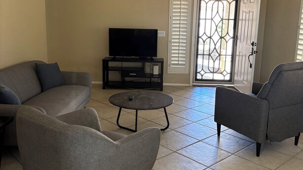 A living room with a ceiling fan, a flat-screen TV on a stand, two grey sofas, a small round table, and a door with decorative glass panels. - 2-bedroom house in wonderful Phoenix with cool AC and comfort (Phoenix)