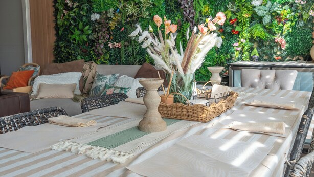 Une pièce avec une longue table à manger, dressée avec des sets de table, une bougie et un panier en osier.