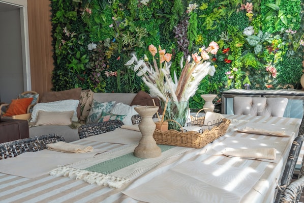 A room with a long dining table set with placemats, a candle, and a woven basket.