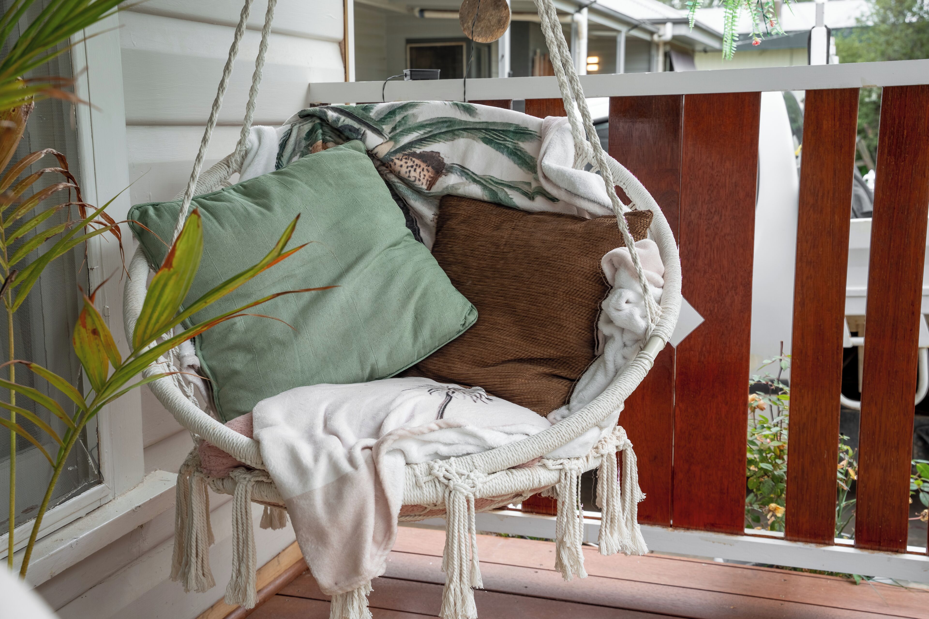 Una silla mecedora de mimbre con cojines, ubicada en una terraza de madera.