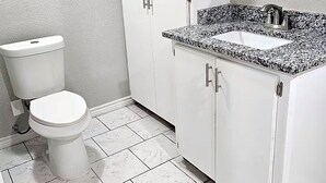 A bathroom with a toilet, white cabinets, a granite countertop, and a mirror.