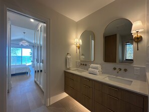 Un baño moderno con lavamanos doble, dos espejos y vistas a un dormitorio con balcón.