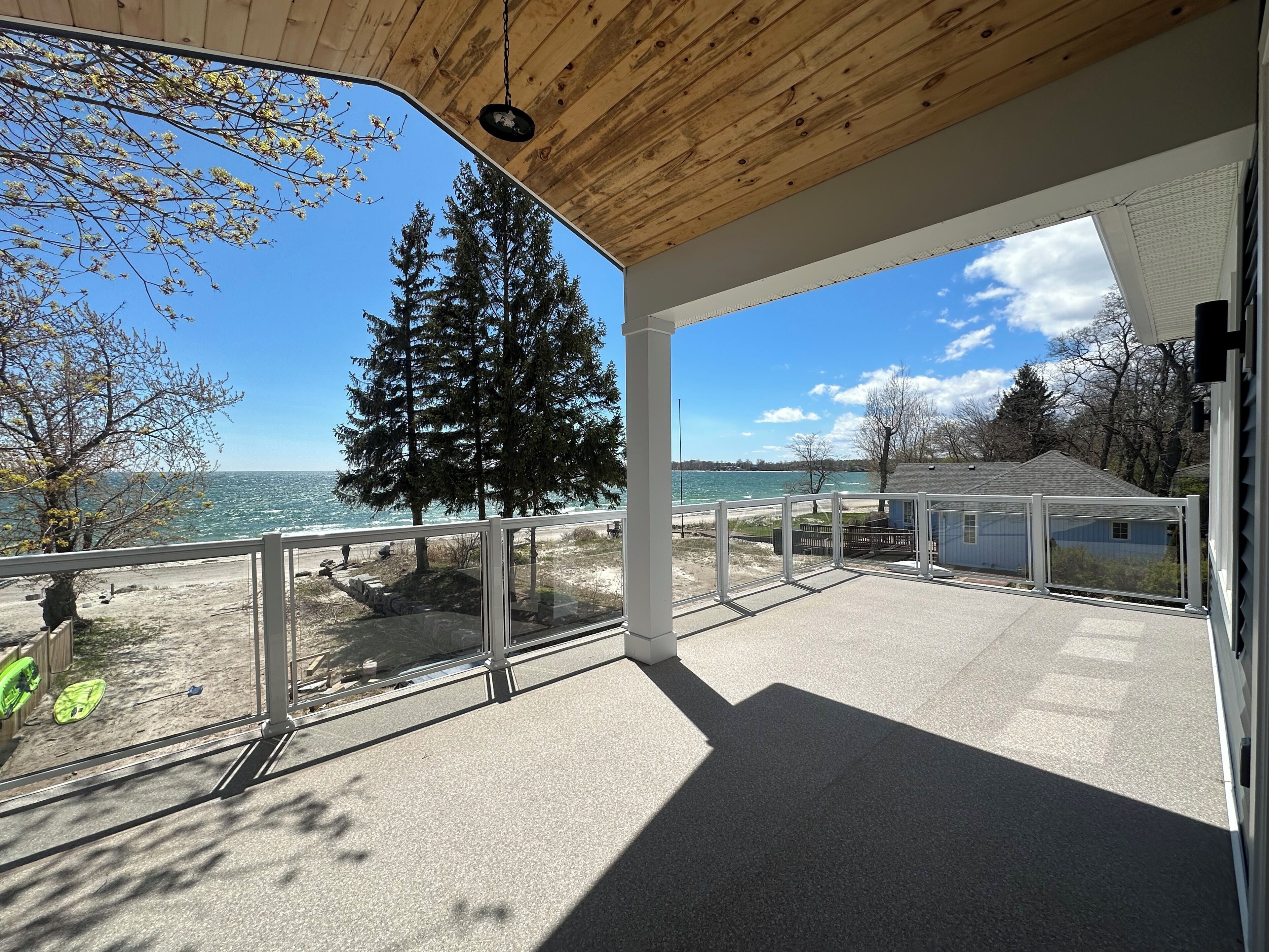 A covered outdoor area with a view of the sea, a large evergreen tree, and a clear sky.
