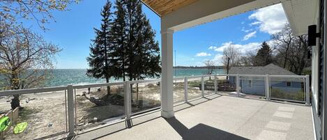 A covered outdoor area with a view of the sea, a large evergreen tree, and a clear sky.