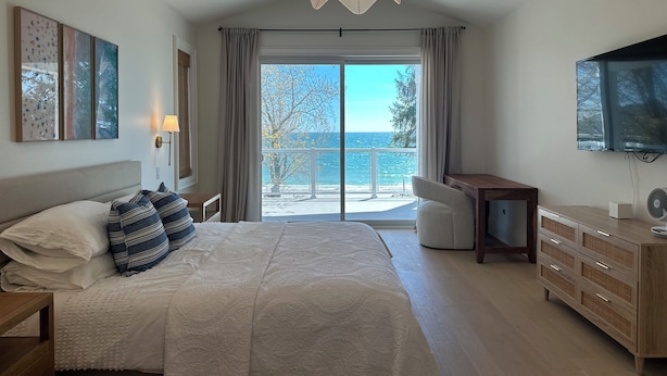 A bedroom with a bed, a desk, a TV, and a view of the sea. - Beachfront Luxury Lake Erie *Sleeps 14* HOT TUB. Great for Hosting Groups (Dunnville)