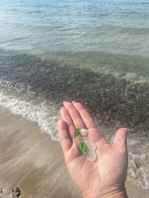 A hand holding a handful of sea glass and a small green object. - Beachfront Luxury Lake Erie *Sleeps 14* HOT TUB. Great for Hosting Groups (Dunnville)