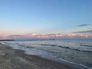 Una playa con un faro a lo lejos, mar tranquilo y cielo despejado.