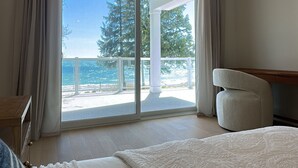 A bedroom with a large bed, a view of the ocean, and a balcony with a wooden deck. - Beachfront Luxury Lake Erie *Sleeps 14* HOT TUB. Great for Hosting Groups (Dunnville)