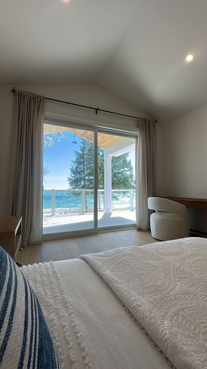 A bedroom with a large bed, a view of the ocean, and a balcony with a wooden deck. - Beachfront Luxury Lake Erie *Sleeps 14* HOT TUB. Great for Hosting Groups (Dunnville)