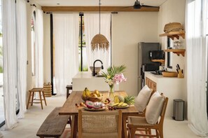 A dining area with a wooden table, wicker chairs, a fruit bowl, and a hanging light fixture. - Casa Degaz Canggu (Canggu)