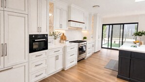 A modern kitchen with white cabinetry, a black oven, a stove, and a large window. - Luxury Country Feel Villa Retreat | Designer Home with elegant features (Wilton)