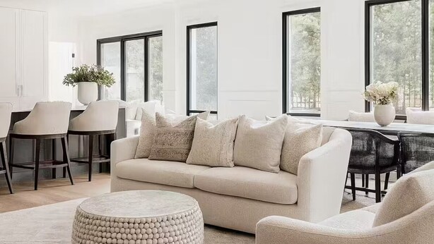 A modern living room with a beige sofa, round ottoman, and dining area with chairs and a table. - Luxury Country Feel Villa Retreat | Designer Home with elegant features (Wilton)