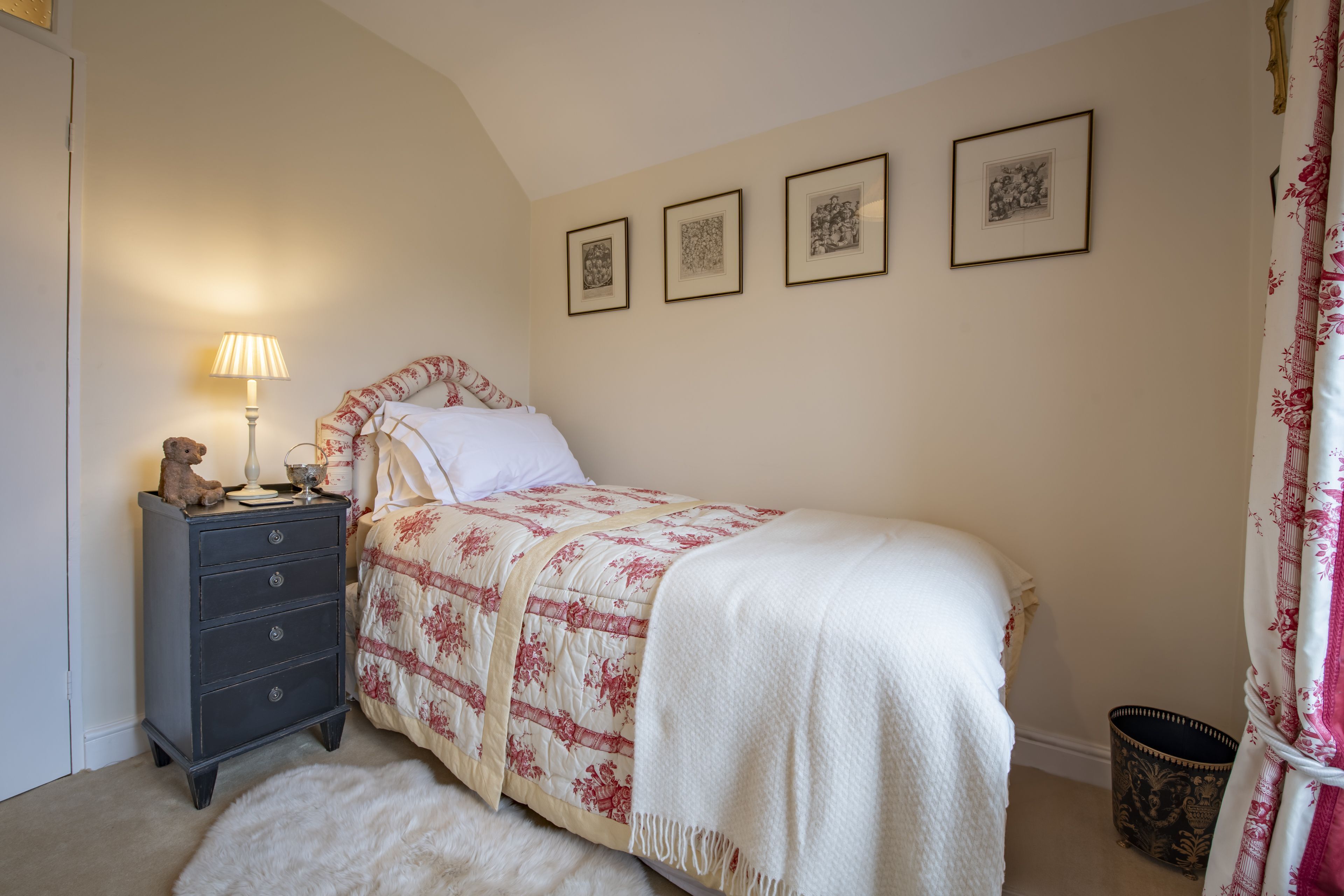 A bedroom with a bed, a dresser, a lamp, a rug, and three framed pictures on the wall.