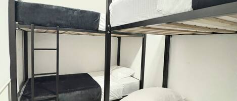 Dormitorio con literas, escalera, ropa de cama blanca y piso de baldosas.
