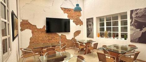 A dining area with glass tables and wicker chairs, a brick wall, a TV, and artwork on the walls.