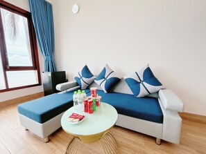 A modern living room with a sofa, a small round table, and a window with curtains. - Song Bien Xanh Resort (Phan Thiet)
