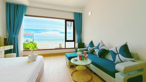 A hotel room with a bed, a sofa, a small round table, and a view of the beach. - Song Bien Xanh Resort (Mui Ne)