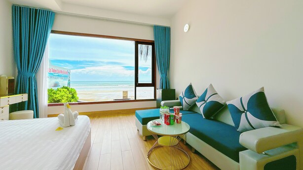A hotel room with a bed, a sofa, a small round table, and a view of the beach. - Song Bien Xanh Resort (Mui Ne)