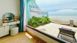 A room with a view of the beach, a poster with hotel information, a mirror, and a small plant. - Song Bien Xanh Resort (Mui Ne)