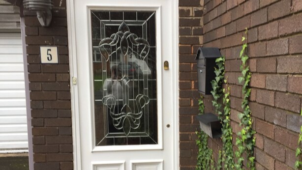 Une porte blanche avec un panneau de verre, un mur de briques, une plaque portant le chiffre « 5 », et une petite marche menant à la porte.