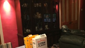 Une table à manger avec une boîte de céréales Harvest Moon Corn Flakes, un bol et une cuillère.