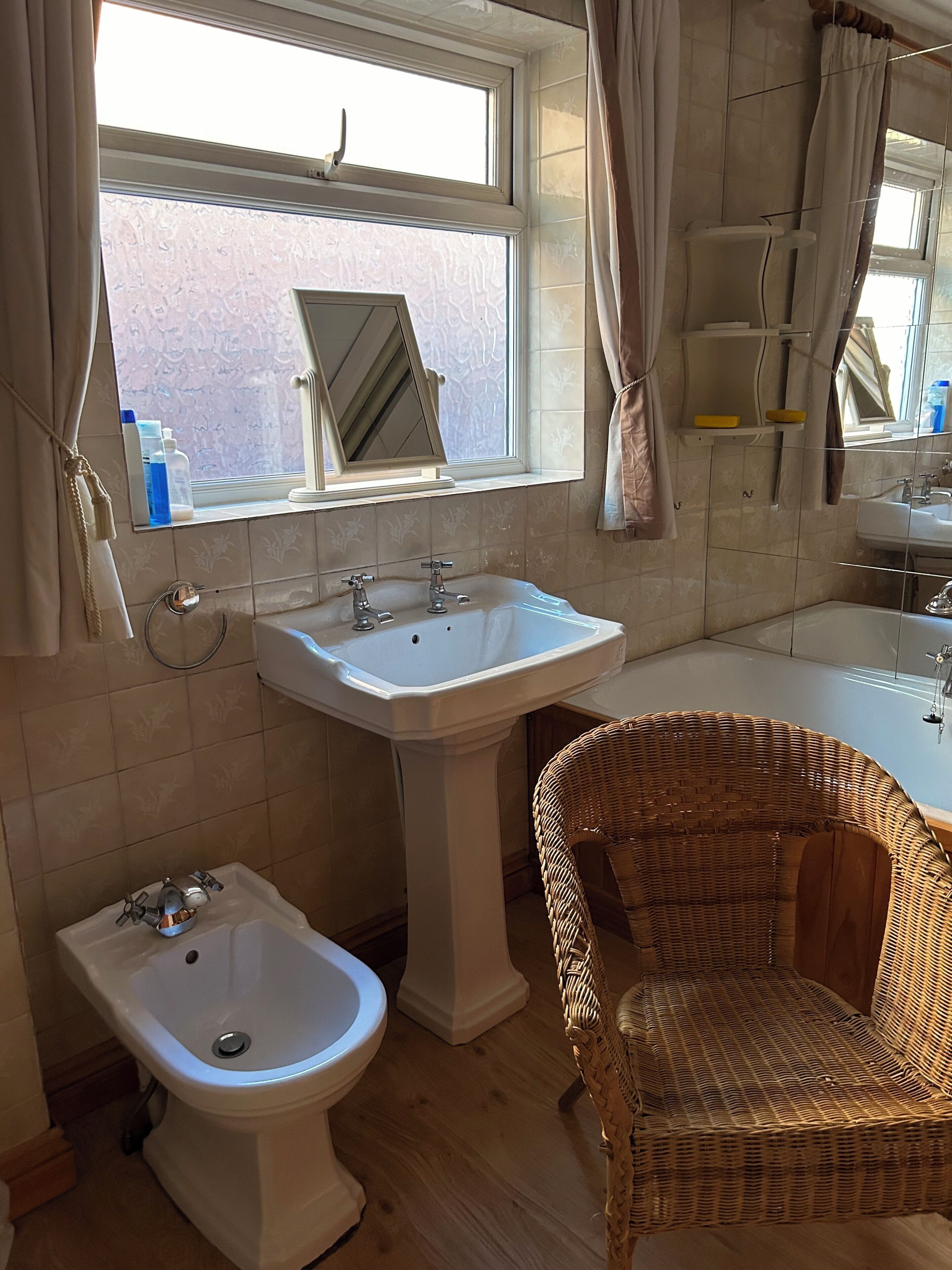 Un baño con un bidé, un lavabo, un espejo y una silla de mimbre.