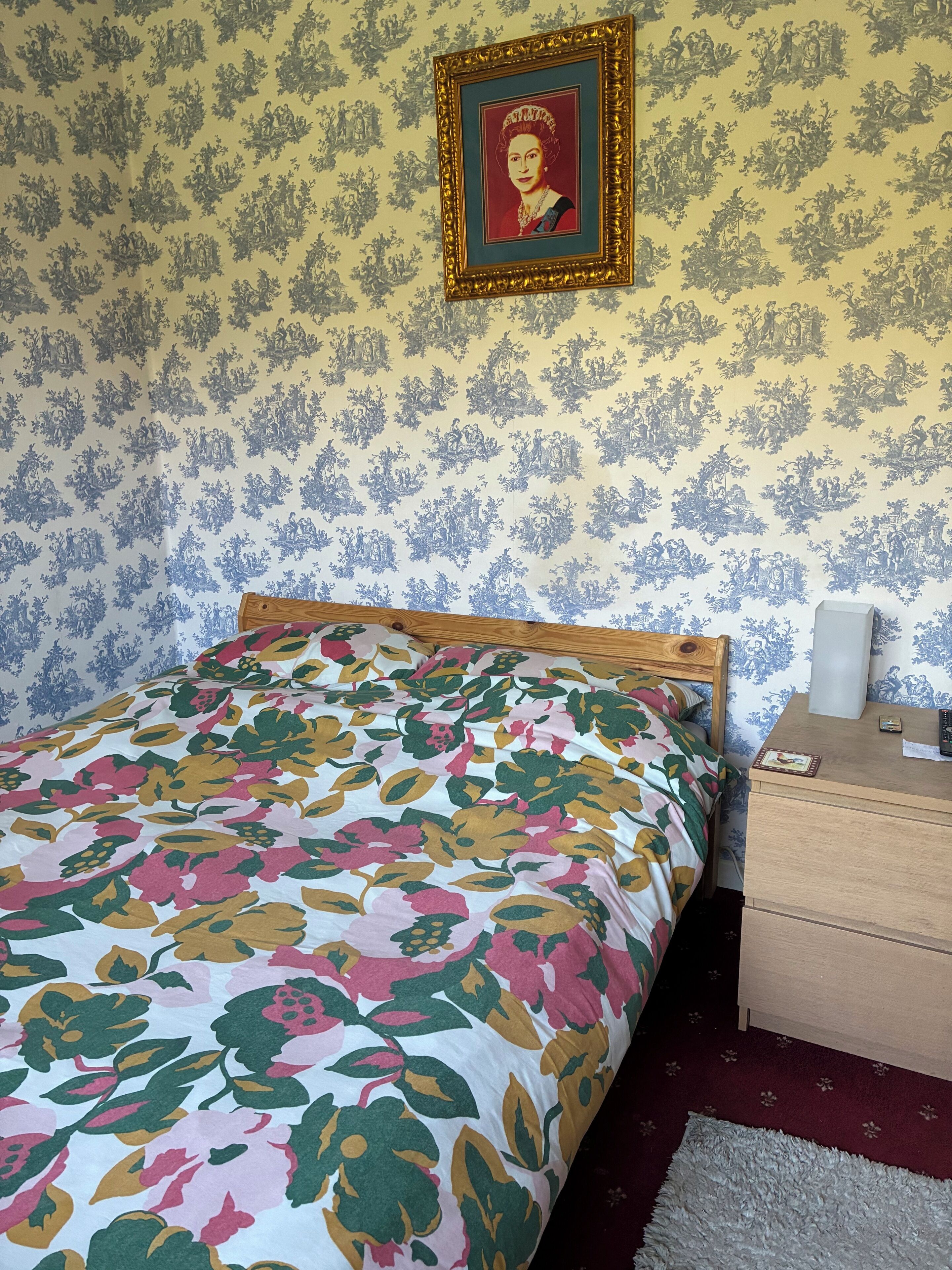 Un dormitorio con colcha estampada, un retrato enmarcado en la pared y una mesita de noche de madera con lámpara.