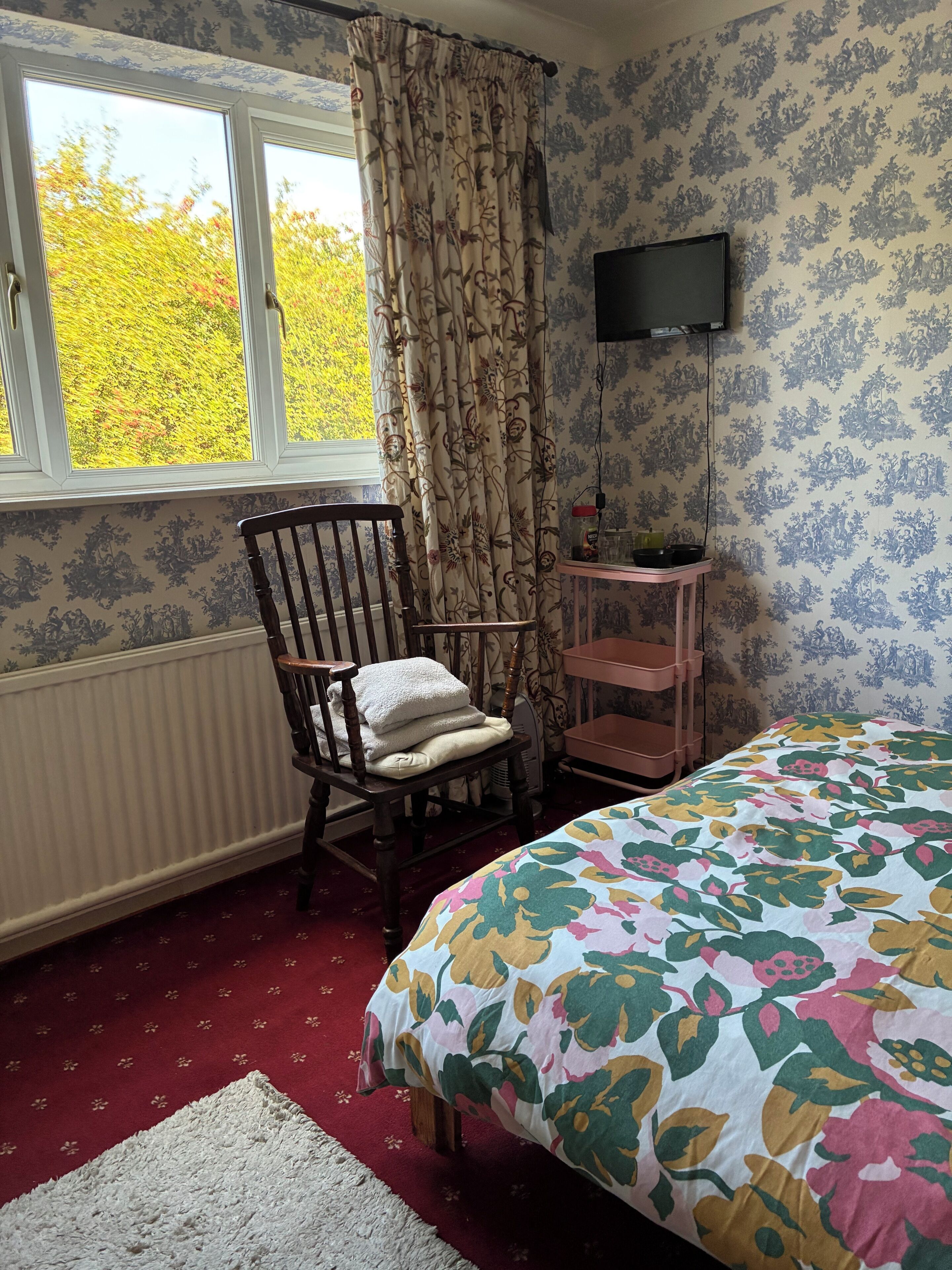 A bedroom with a bed, a chair, a radiator, a TV, and a window with curtains.