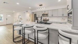 Una cocina moderna con encimera de mármol, electrodomésticos de acero inoxidable y taburetes de bar.