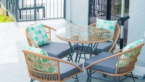 A balcony with wicker chairs and a glass table, a white umbrella, and a view of the sea. - Luxury 3 BR, Ocean view, With Pool, 15 mins from POS (Carenage)