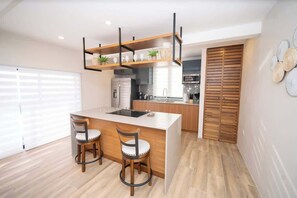 Eine moderne Küche mit einer zentralen Kochinsel, zwei hölzernen Stühlen, einem eingebauten Backofen und einer Holztür.